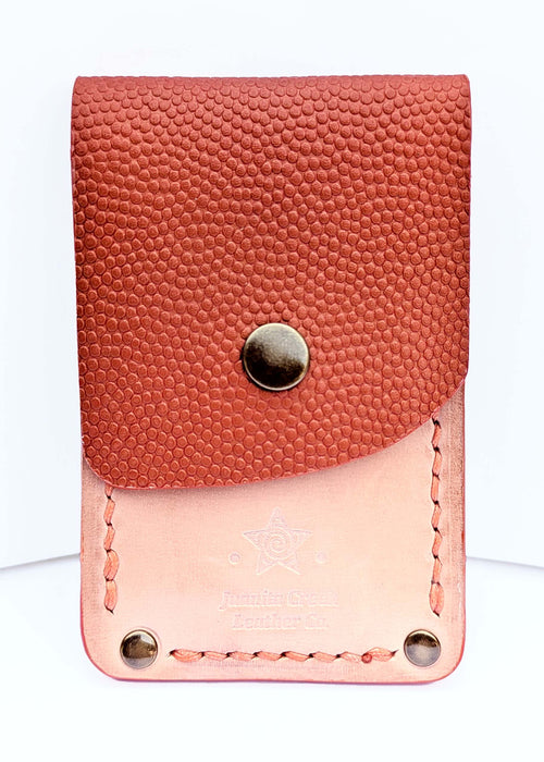 A small leather card holder or wallet with a textured reddish-orange pebbled flap and a smooth blush pink body, featuring a snap button closure and visible stitching.