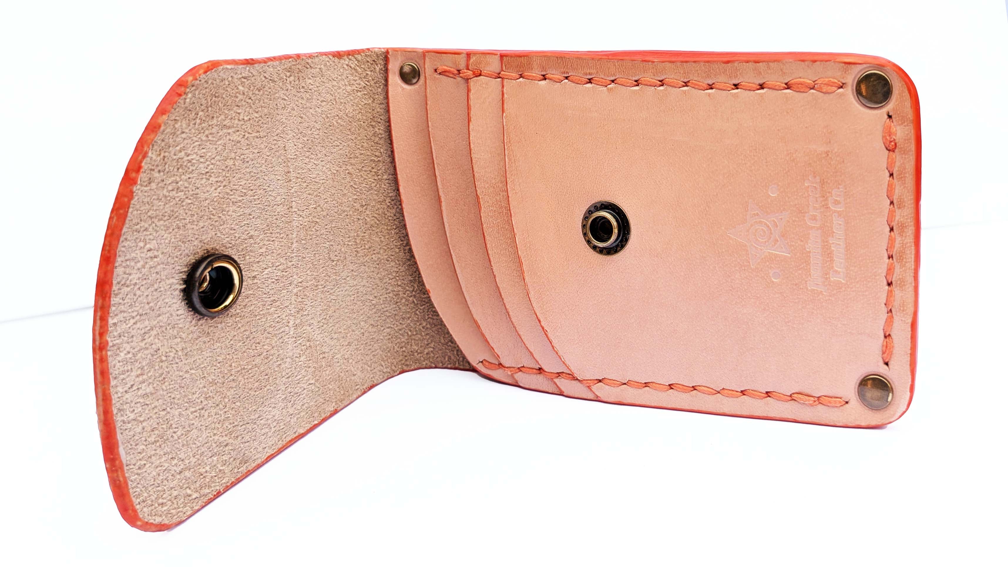A light peach leather card holder wallet shown open, displaying its interior card slots, tan lining, orange-red stitched edges, and brass snap button closures on a white background.