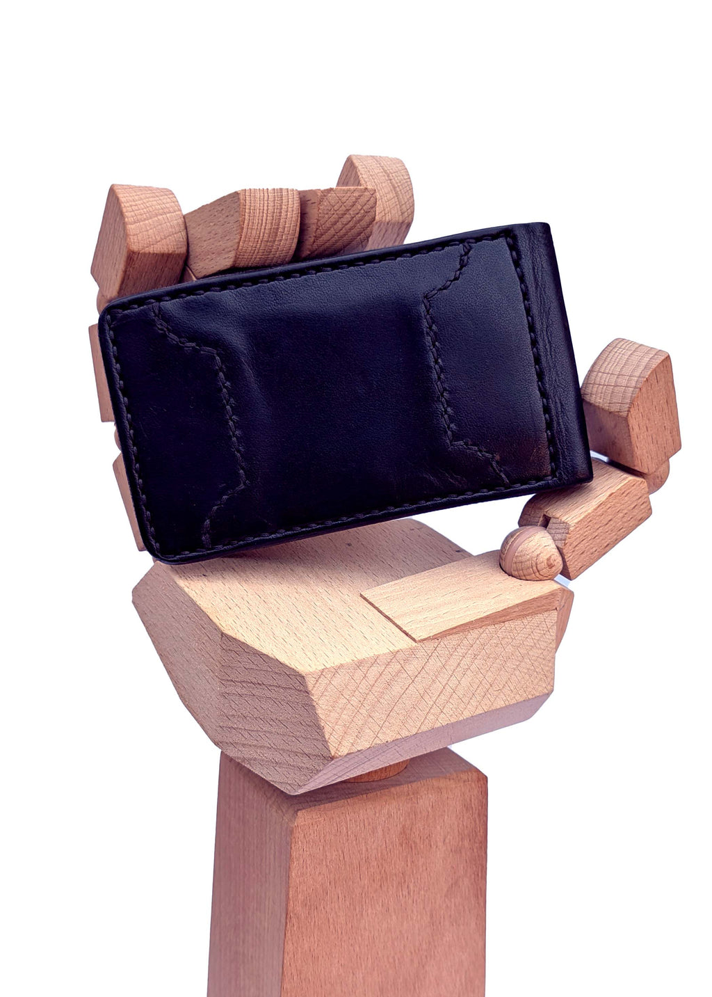 A black leather wallet or card holder with visible stitching, held by a stylized wooden hand sculpture against a plain white background.
