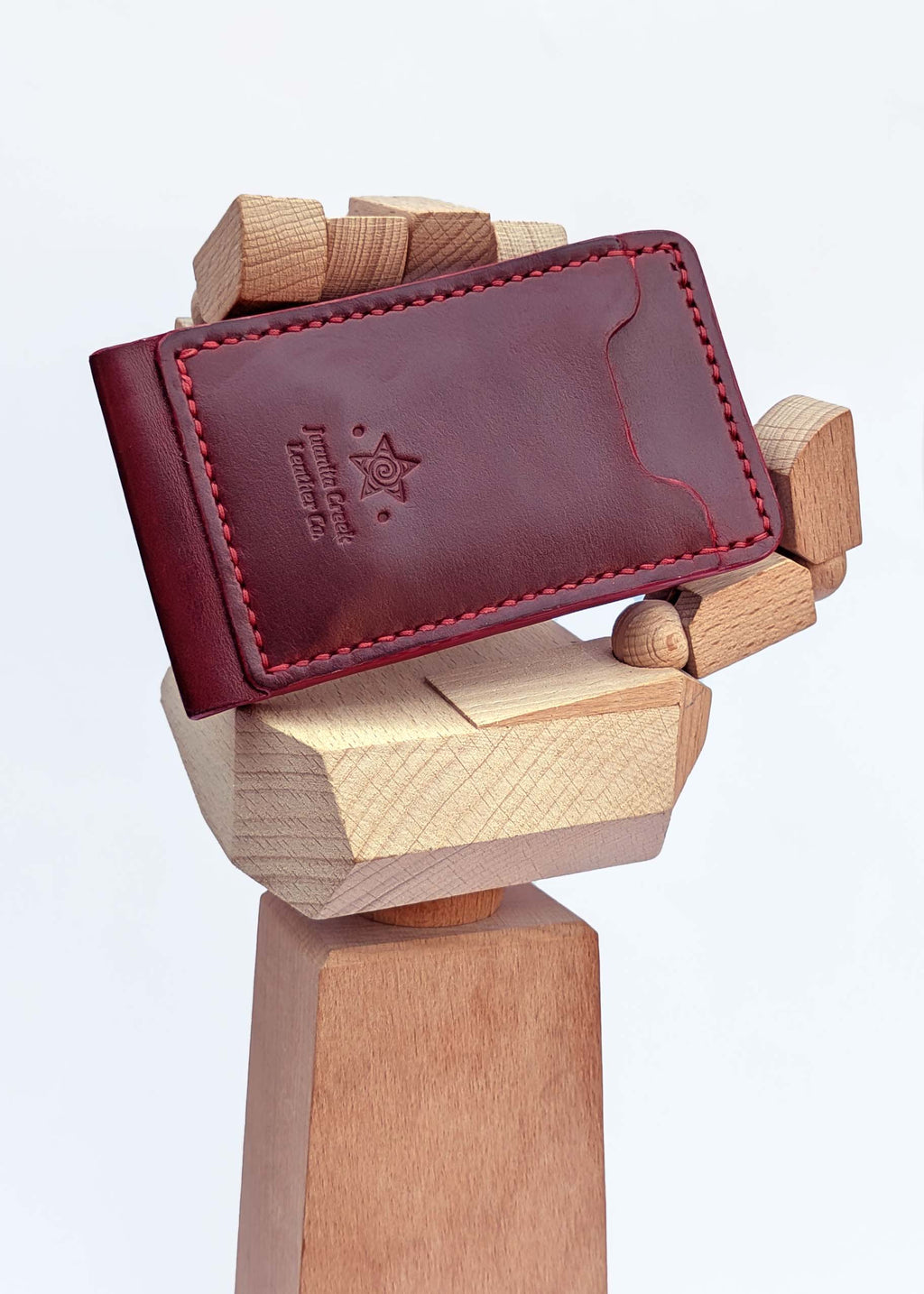A dark red leather card holder wallet with red stitching and an embossed logo, displayed on a wooden stand against a white background.