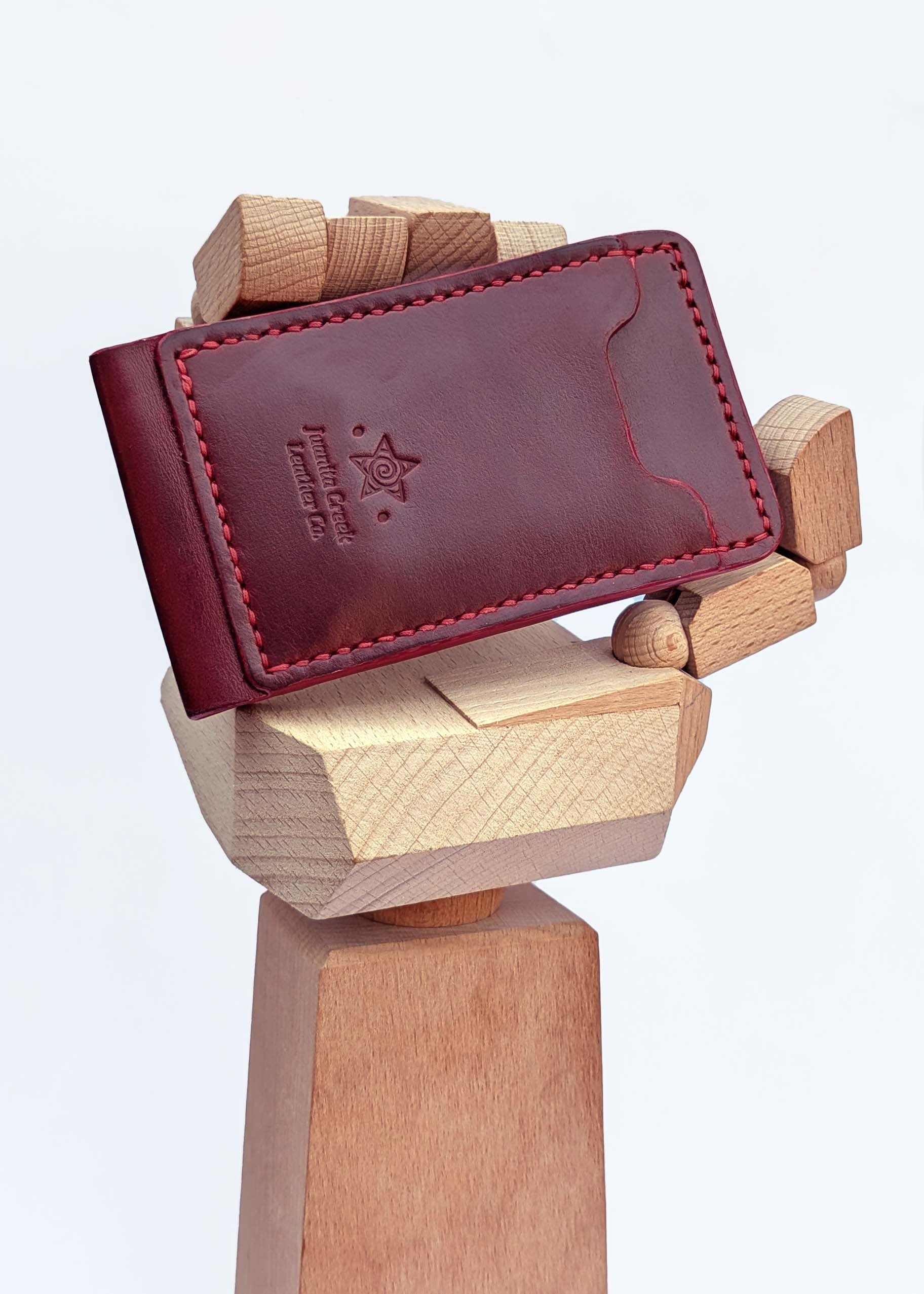A dark red leather card holder wallet with red stitching and an embossed logo, displayed on a wooden stand against a white background.